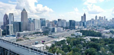 An image of a skyline under blue skies near a huge highway with many trees and smaller buildings at bottom. 