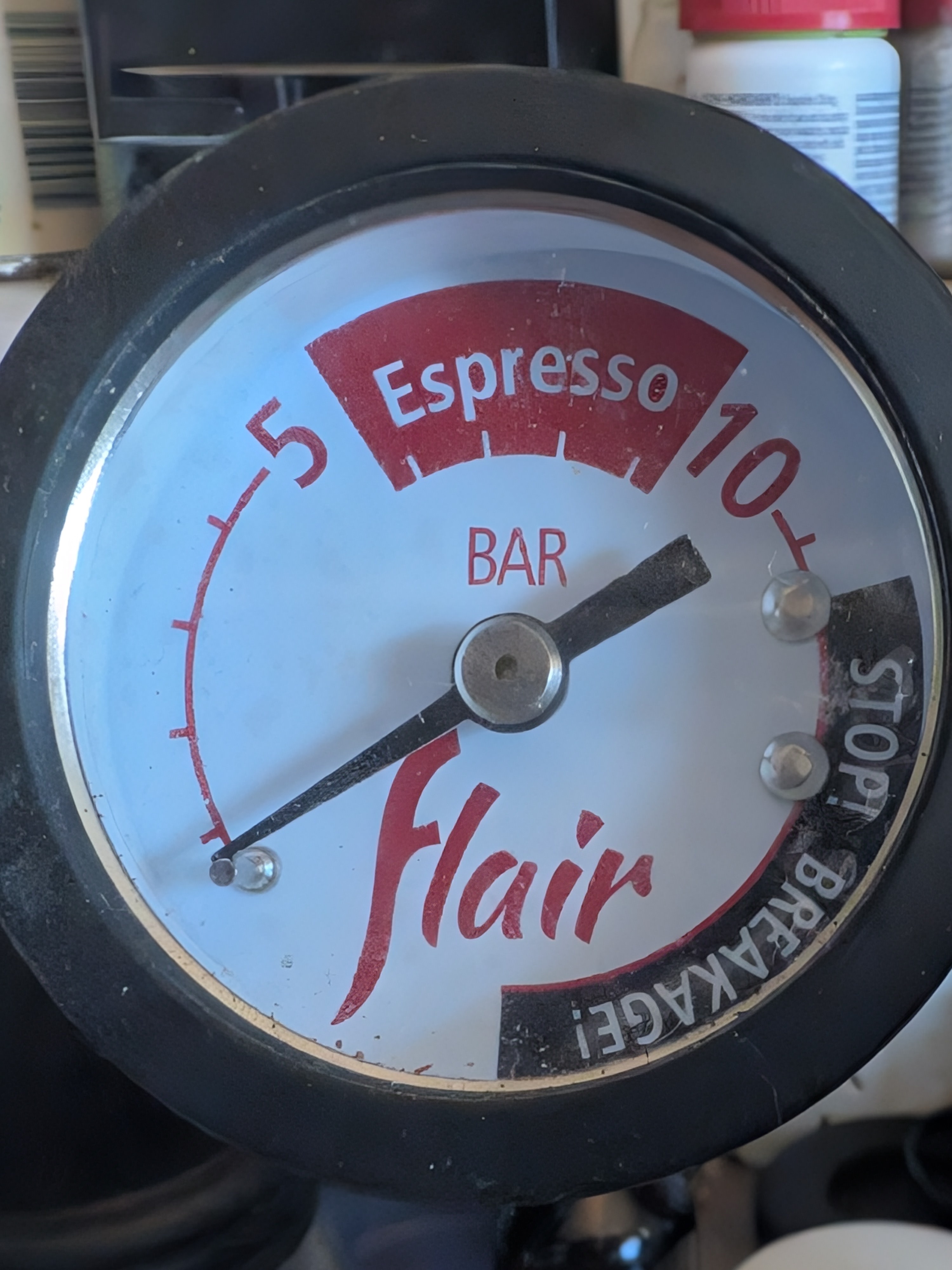 Flair 58 lever coffee machine's pressure gauge marked as showing pressure in bar with tick marks for each bar and numbers at 5 and 10 bar. A red area between 5 and 10 is labeled 'Espresso". A black area from 12 bar onwards is labeled  'STOP! BREAKAGE!"