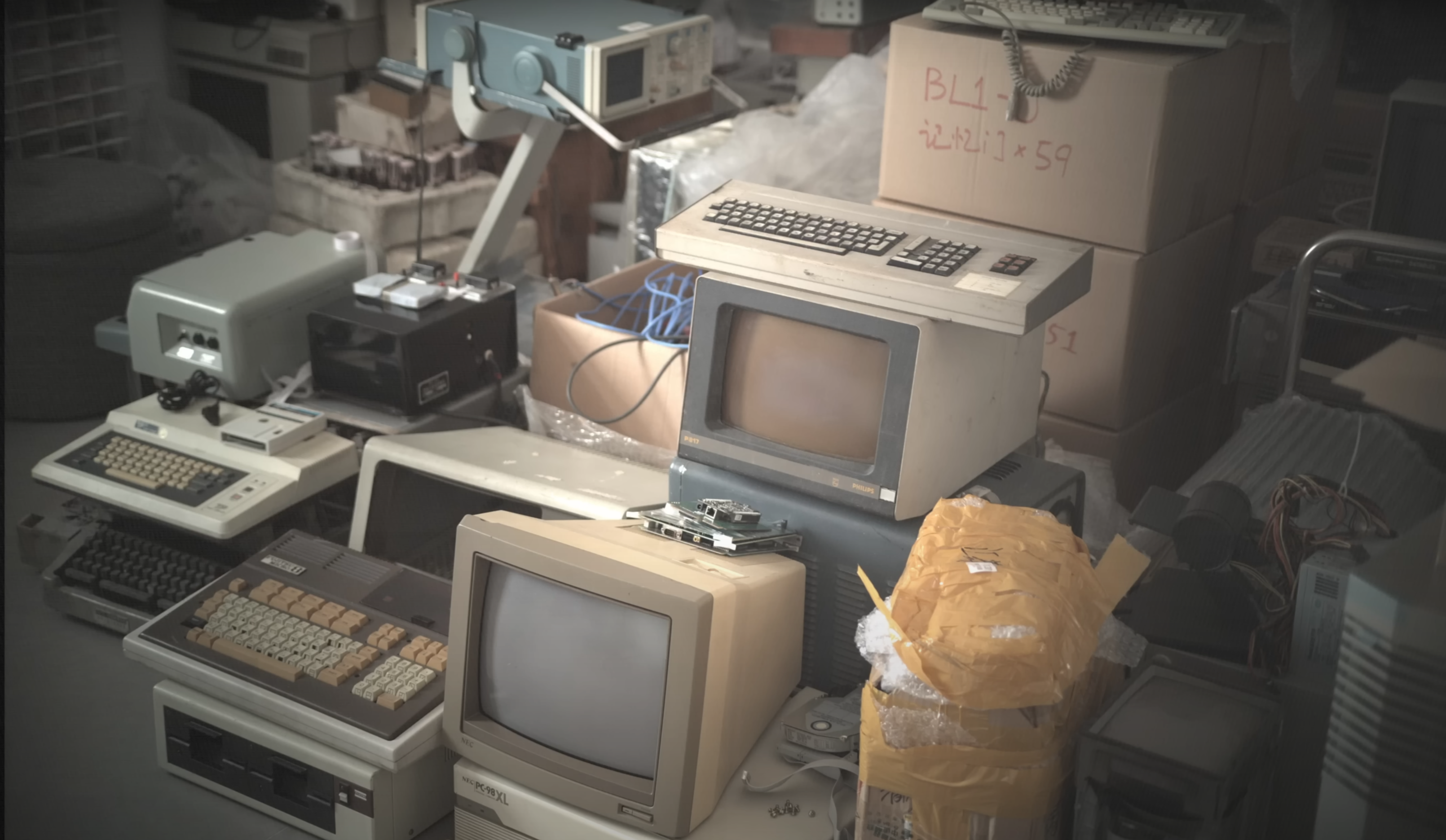 Colour photo of piled up old computers and computer peripherals from the grey/beige era. The colours are muted but not completely desaturated. It resembles film more than the average post-processed digital photo