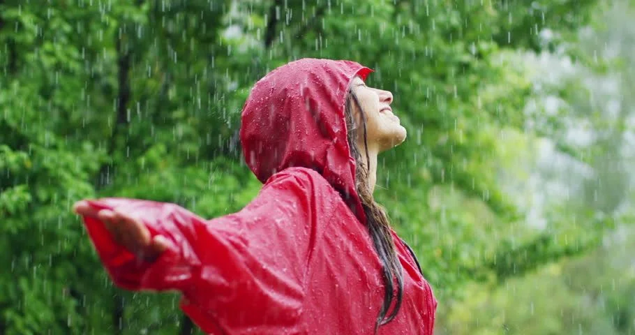 Eine Frau mit Regenumhang steht lächelnd im Regen