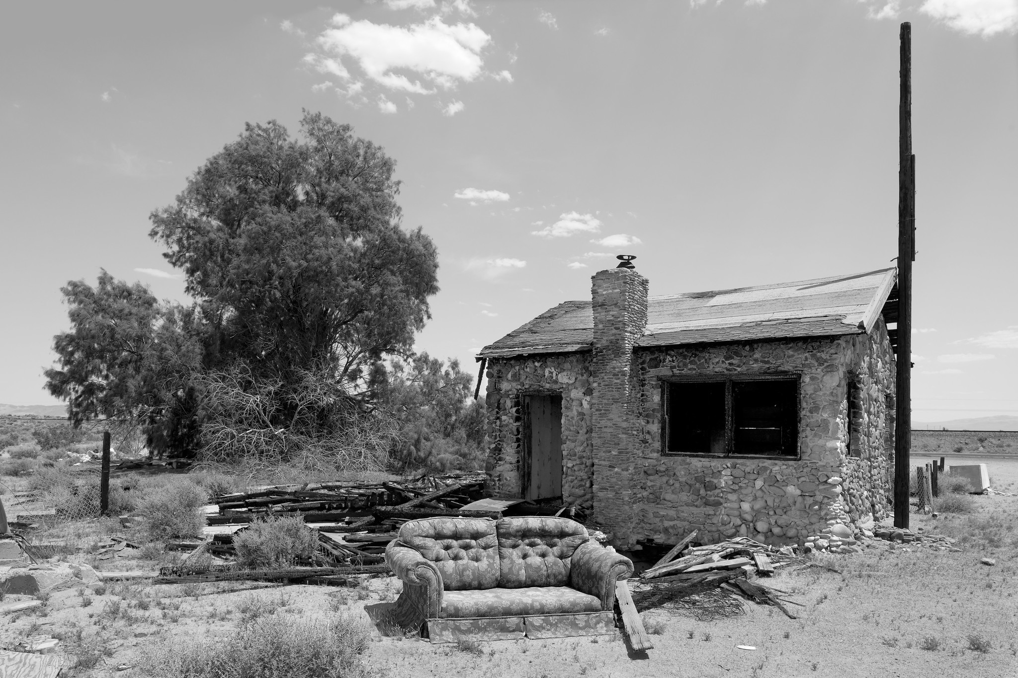 A simple one room stone house, apparently damaged by fire, with a couch sitting in front.