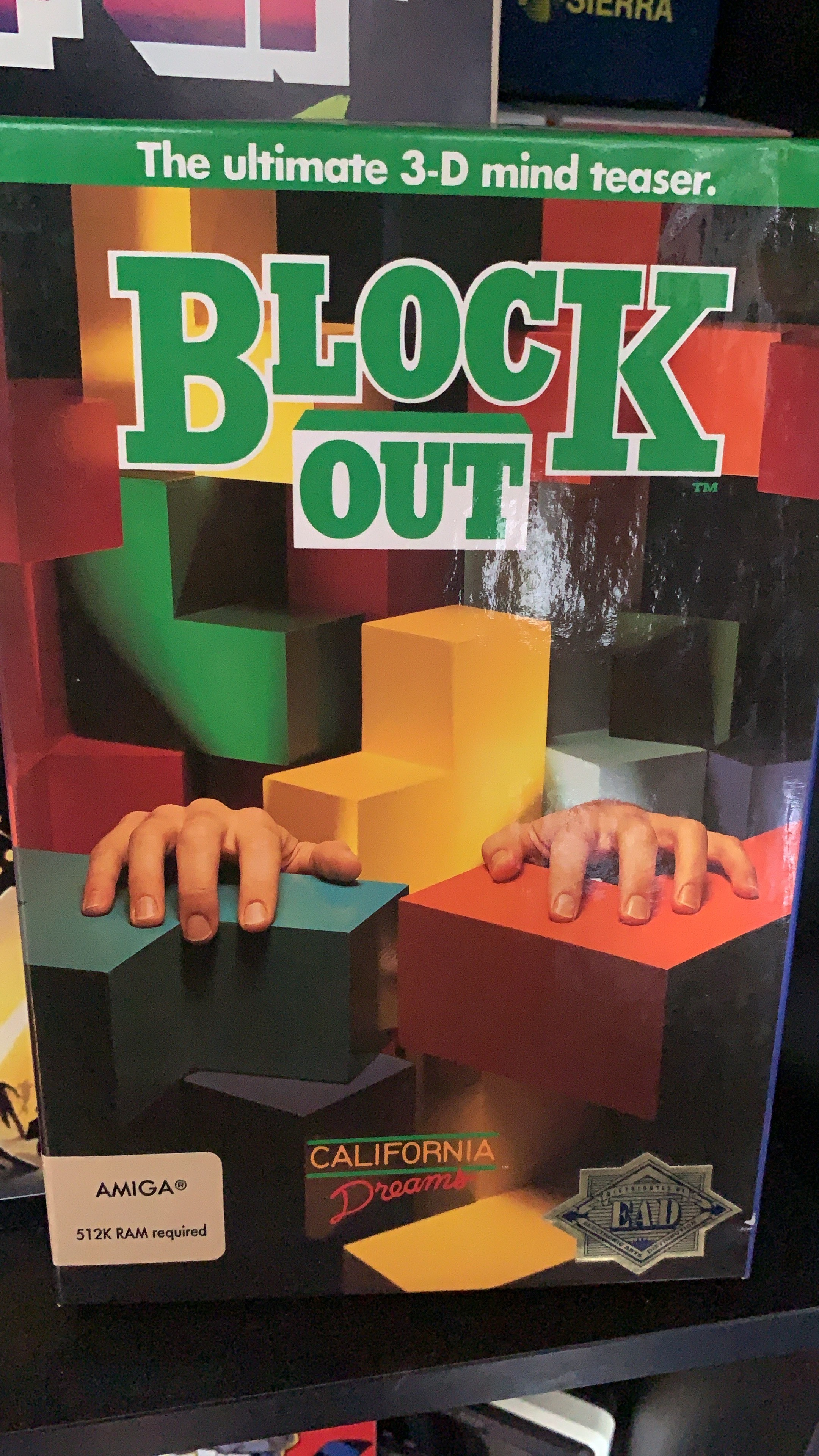 The game‘s box but for the Amiga. Many 3D Tetris shapes are stacked on top of each other, with hands clinging to one of them, suggesting the player being overwhelmed. 