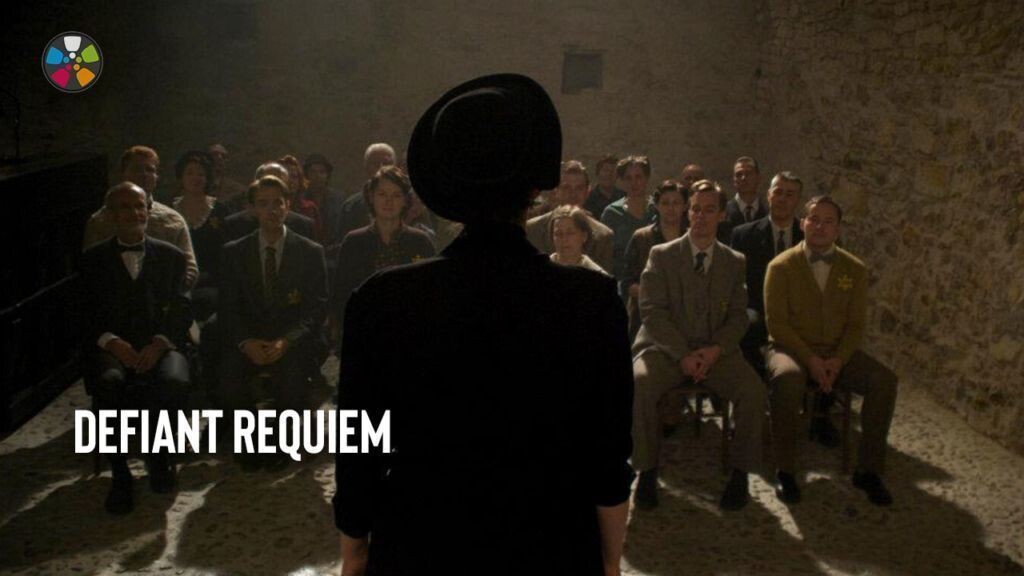 Still photo from Defiant Requiem: a person shown in silhouette from the back addresses a group of people seated on rows of wooden chairs in a barren room.