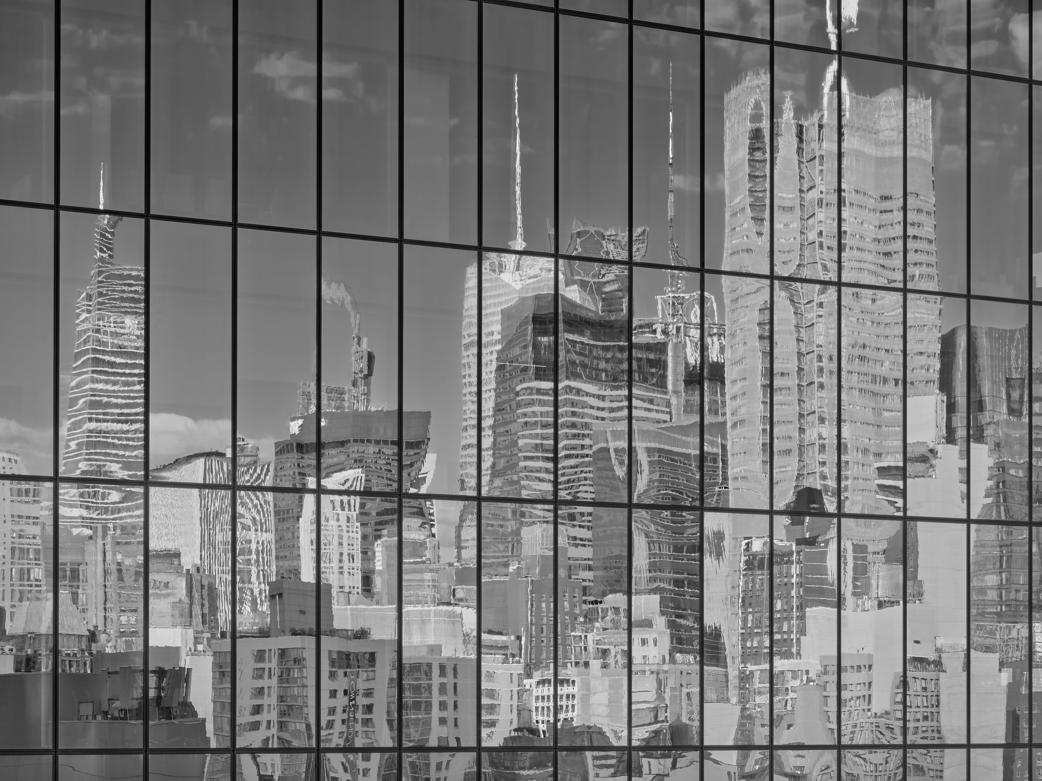 Detail of the side of a glass curtain office building, with a grid formed by window sections, showing a distorted reflection of a crowded skyline of skyscrapers.