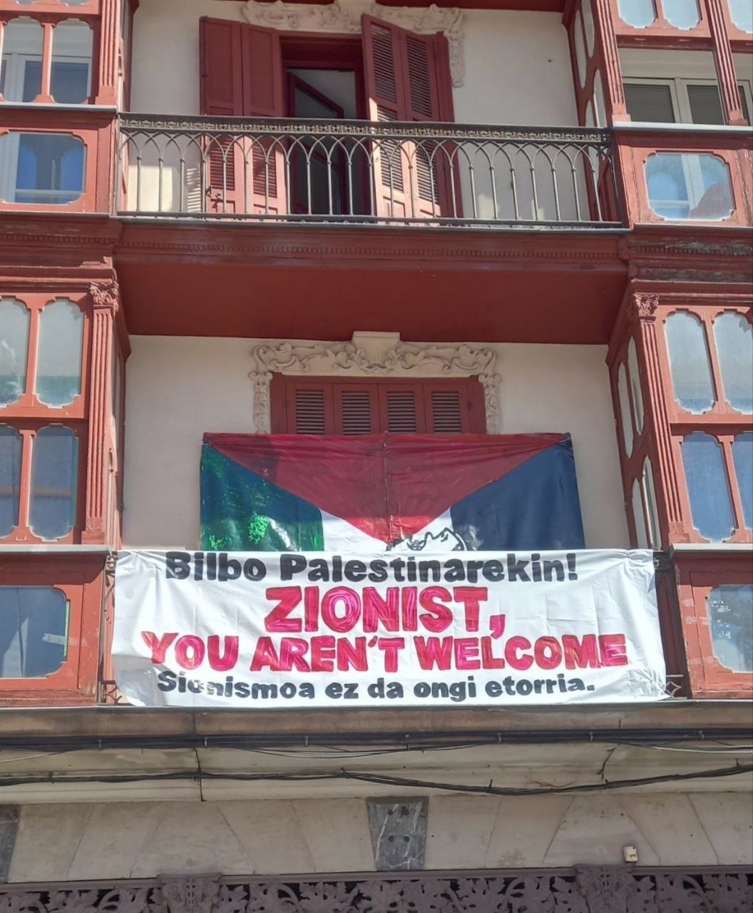 Banner on a balcony reads "Zionist, you aren't welcome"